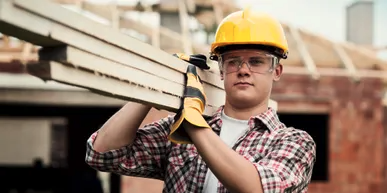 A man in yellow hard hat holding wood.